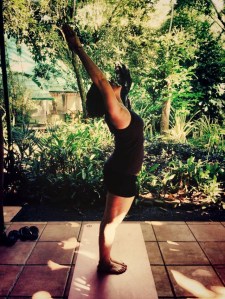 Rachel, practicing yoga, stands in mountain pose with a gentle back bend. Courtesy of Rachel Kellogg.