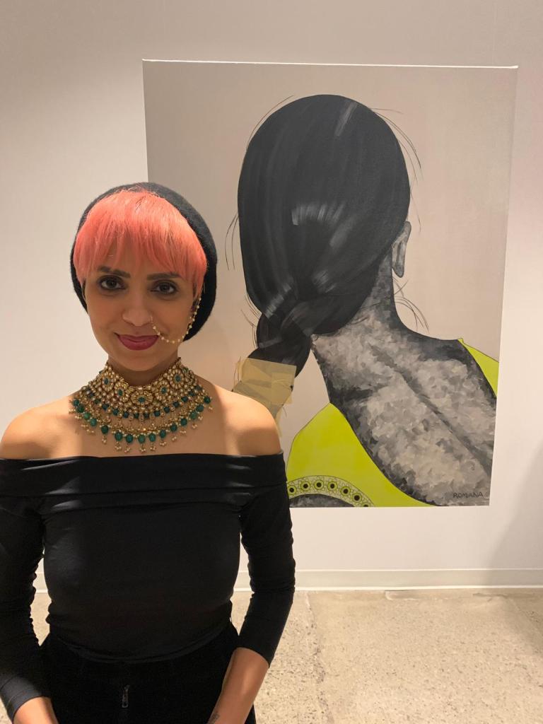 Romana Kassam stands in front of an art piece she made, displayed at her first solo exhibition, MasksxMolds. Photo by: Alim Alarakhia.